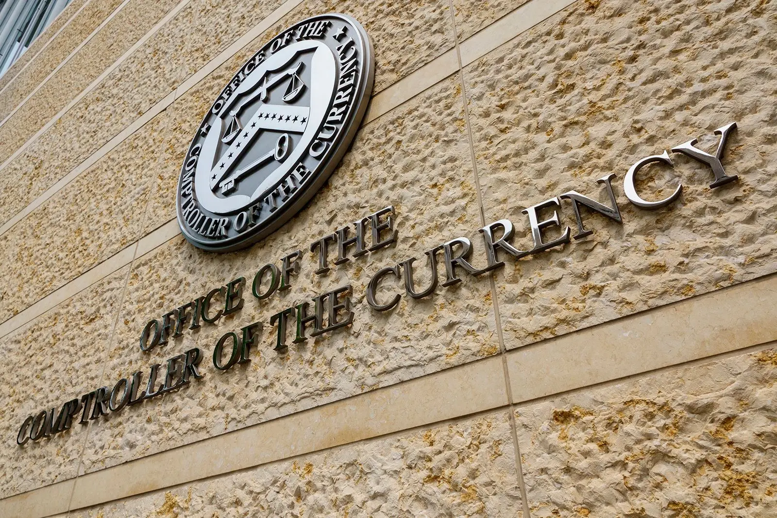 Close-up of the Office of the Comptroller of the Currency seal and lettering on a stone wall